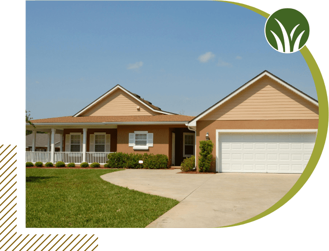 A single-story house with a tan exterior, white garage door, white porch railing, and a neatly manicured lawn under a blue sky.